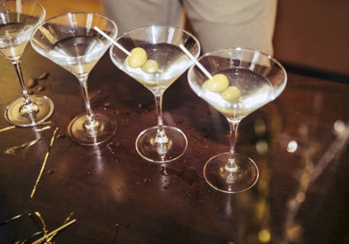 Five martini glasses with olives on a dark surface, ready for serving.