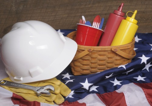 A white hard hat, wrench, gloves, basket with condiments, and utensils on an American flag-themed cloth.