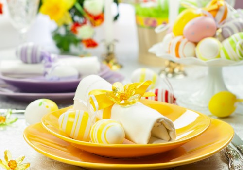 A festive table setting with decorated Easter eggs, napkins, and flowers on colorful plates, perfect for a spring celebration.