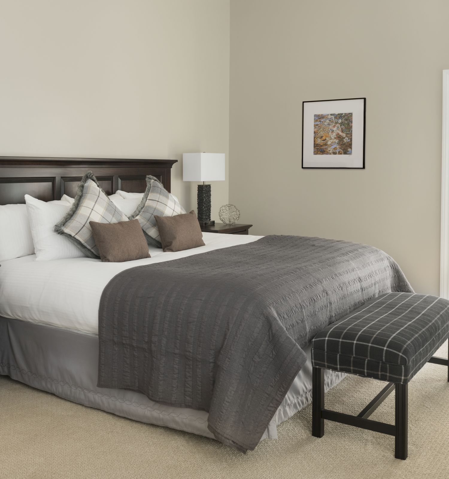 A bedroom with a large bed, two nightstands with lamps, a bench at the foot of the bed, and a door leading to a balcony.