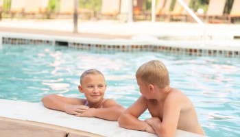 Two kids are at the edge of a swimming pool, chatting and having fun.